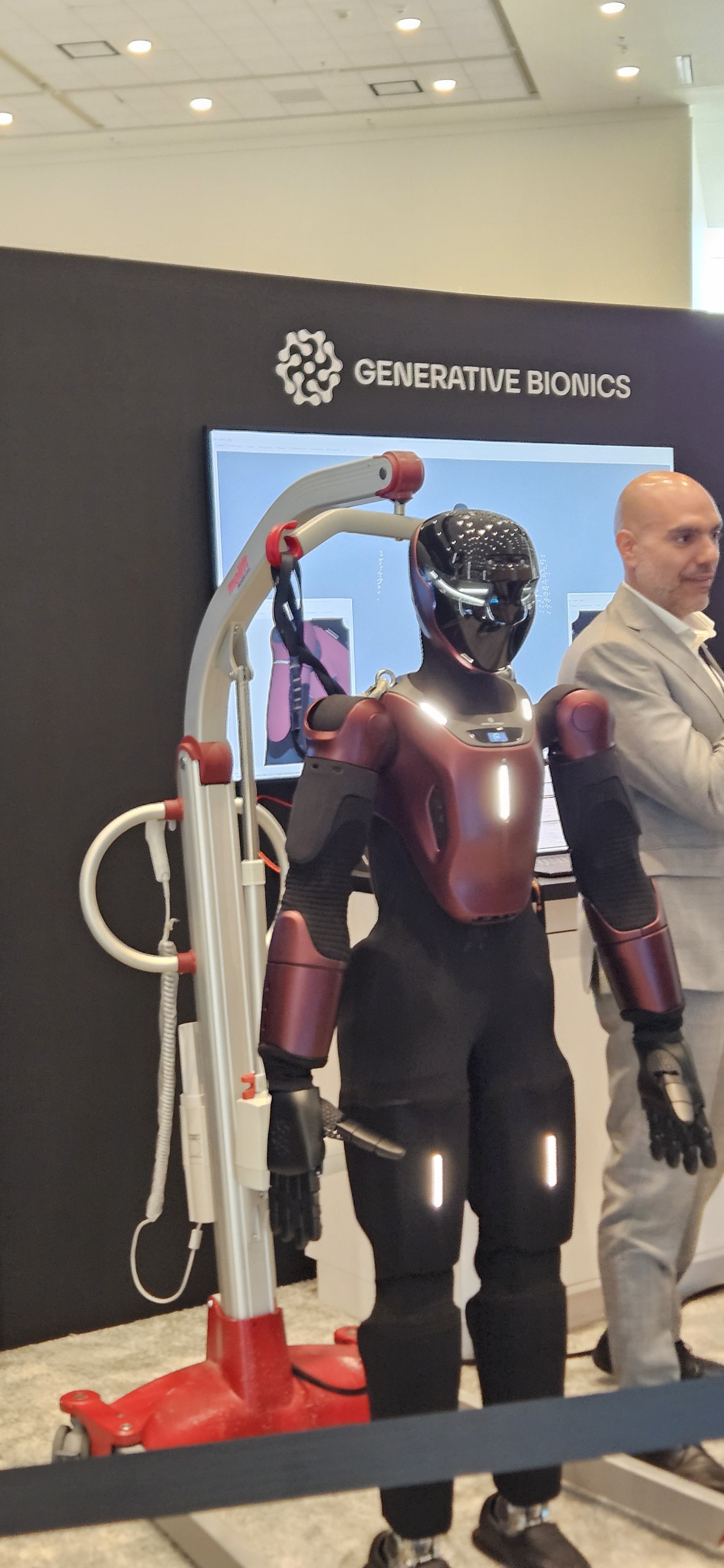 A Generative Bionics humanoid robot on a support gantry at the Advancing AI 2026 show floor, with visible actuated arms, hands, and a sensor-covered head.