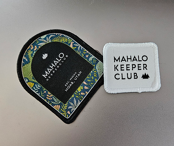 Two Mahalo Keeper Club patches: an embroidered arch-shaped patch with a floral border reading Mahalo Keeper Club, Est. MMXX, Moab, Utah, and a simpler white patch reading Mahalo Keeper Club with a mountain icon.